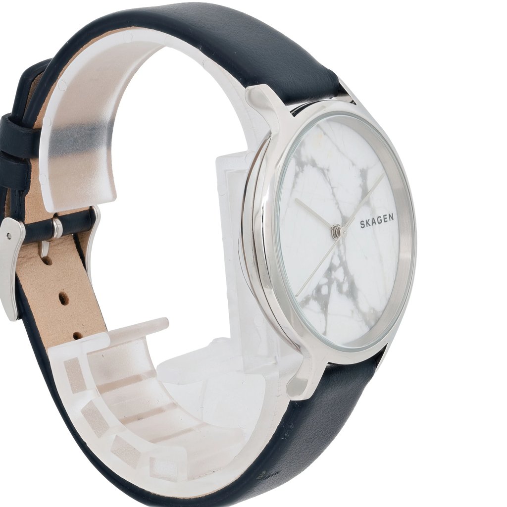 An image of a Skagen women's wristwatch, new with defects, displayed at a slight angle from the front. The watch features a marble-patterned face with a minimalistic design and a silver-toned bezel. The black leather strap is partially visible, wrapped around a transparent stand. The brand name "Skagen" is visible on the watch face. The photo is taken from a close distance, capturing the details of the watch's design.