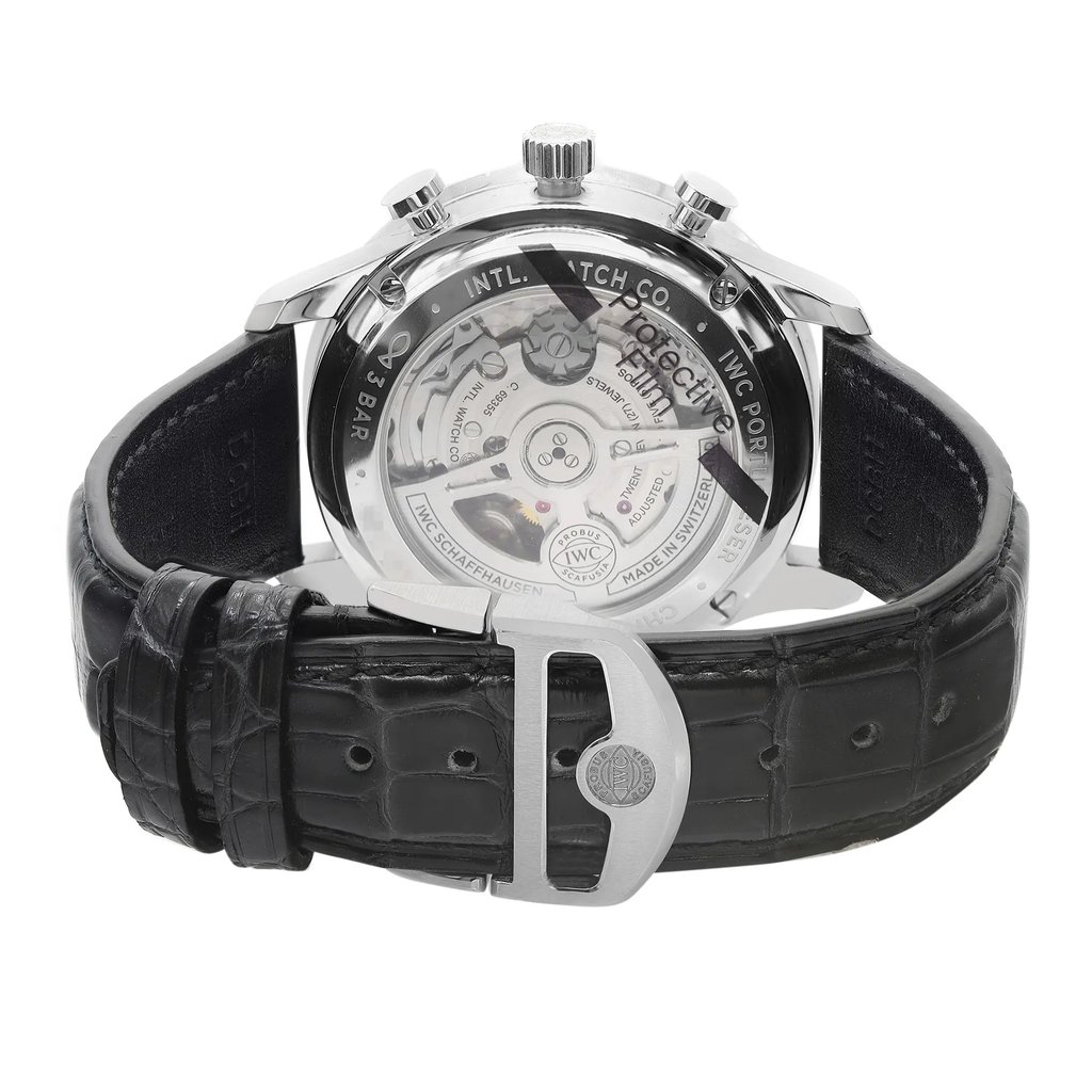 An image of an unworn IWC men's wristwatch with a stainless steel case and an exhibition caseback, viewed from the back at a slight angle. The round watch is attached to a black leather band with a deployant closure, and the clasp is prominently displayed in the foreground. The photo is taken up close, capturing the intricate details and textures of the watch's design.