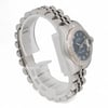 An image of a pre-owned women's Rolex wristwatch, positioned at a three-quarter angle, highlighting its silver bracelet and dark watch face with luminous hands. The watch is viewed from a close-up distance, showcasing its intricate details, including the fluted bezel and Roman numerals.