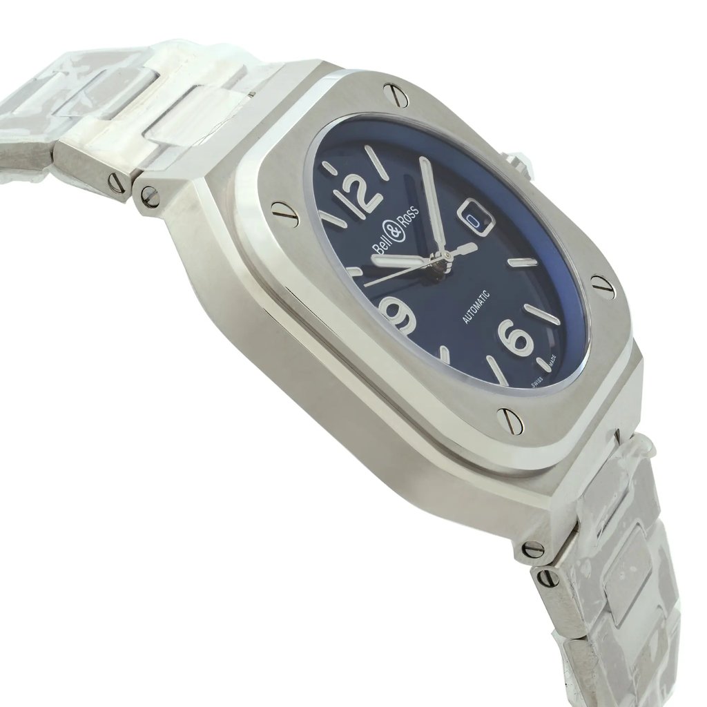 An image of a Bell & Ross men's wristwatch in a display model condition, showcasing a side profile view opposite of the crown. The watch features a luxurious dress/formal style with a blue dial color, a cushion-shaped stainless steel case, and a stainless steel band. The watch is positioned at a slight angle, with the face clearly visible and the band extending away from the viewer, creating a sense of depth. The photo is taken from a close distance, emphasizing the watch's design details and brand markings.