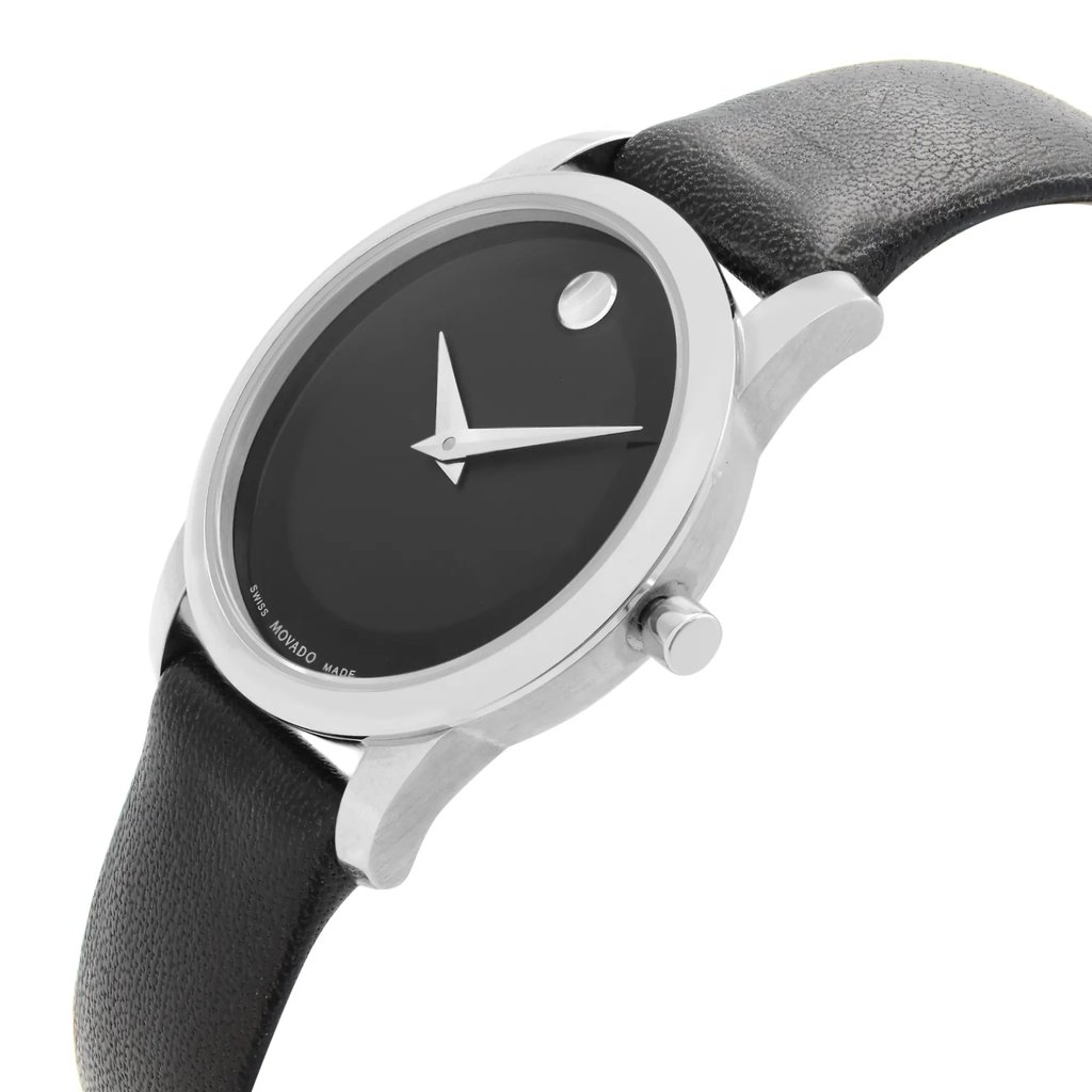 An image of a pre-owned wristwatch shown from a side profile view, highlighting the crown. The watch features a sleek black dial with minimalistic silver hands and a single dot at the 12 o'clock position. The case is silver-toned, complemented by a textured black leather strap. The angle captures the watch at a slight upward tilt, emphasizing its elegant design and craftsmanship.