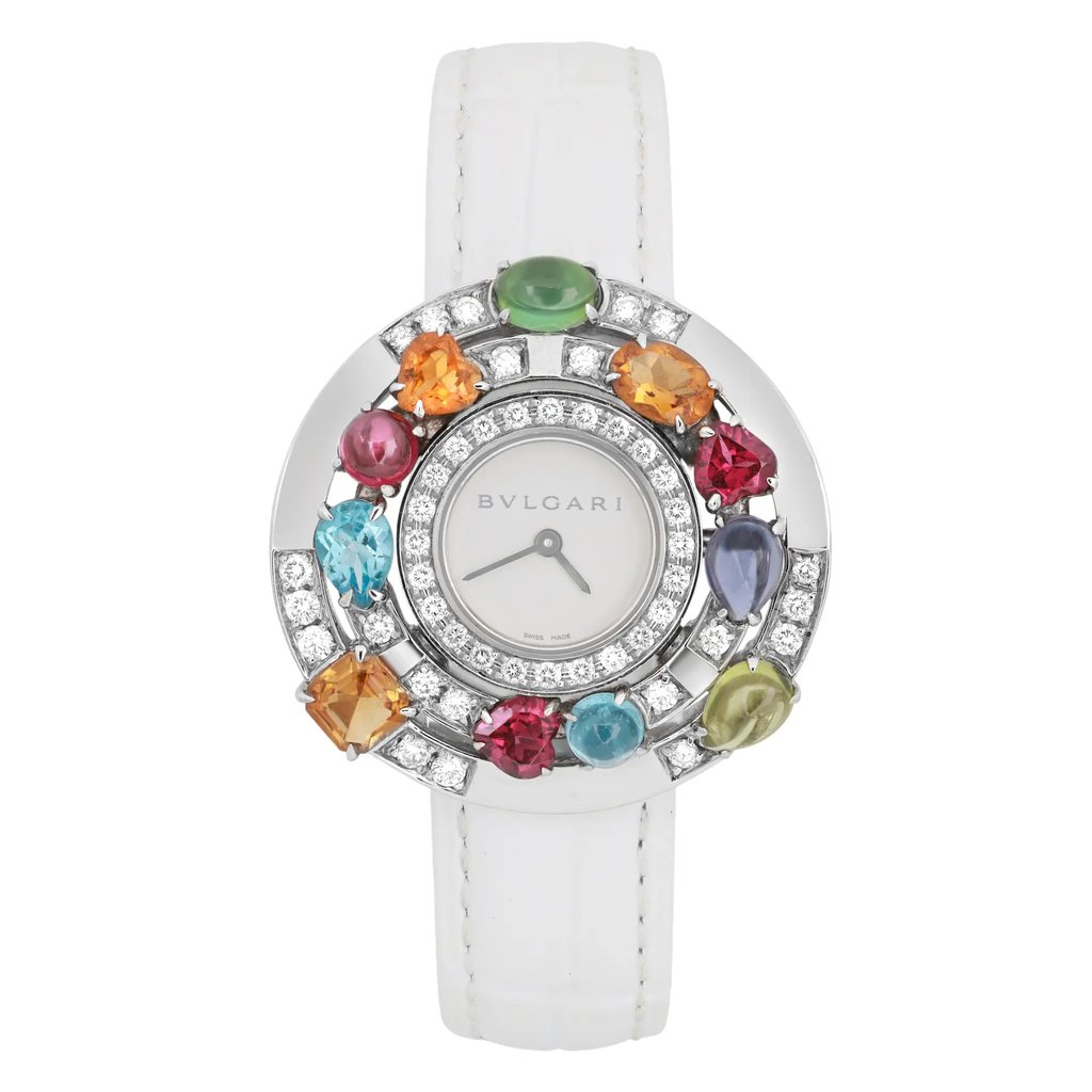 An image of a pre-owned Bvlgari Astrale Gemed Diamond 18K White Gold White Leather Watch 101338 shown from a straight-on angle. The watch features a white strap and a round silver-toned face adorned with colorful gemstones and diamonds around the bezel. The brand name "Bvlgari" is visible on the dial. The vibrant stones include shades of orange, red, green, blue, and yellow, adding a luxurious and eye-catching detail to the timepiece. The image captures the watch in a close-up view, highlighting its intricate design and elegant craftsmanship.