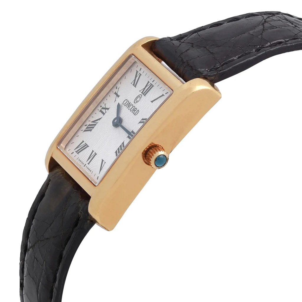 An image of a pre-owned wristwatch viewed from the side profile angle, focusing on the crown. The watch has a rectangular gold case and a black leather strap. The face displays Roman numerals and the brand name. The crown is prominently visible, featuring a blue accent. The angle highlights the watch's sleek design and details.