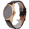 An image of a pre-owned men's GUESS wristwatch, positioned at a slight angle, showcasing the side and partial front view. The watch features a rose gold-tone case and a textured dark brown leather strap. The dial is dark with minimalist hour markers. The image is taken at a close distance to highlight the details and craftsmanship of the watch.
