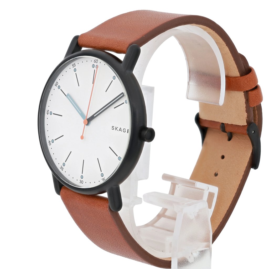 An image of a men's Skagen wristwatch displayed at a three-quarter angle. The watch features a white dial with minimalist black hour markers and luminous hands. It has a brown leather strap and a black case, positioned upright on a clear stand, showcasing its design and craftsmanship.