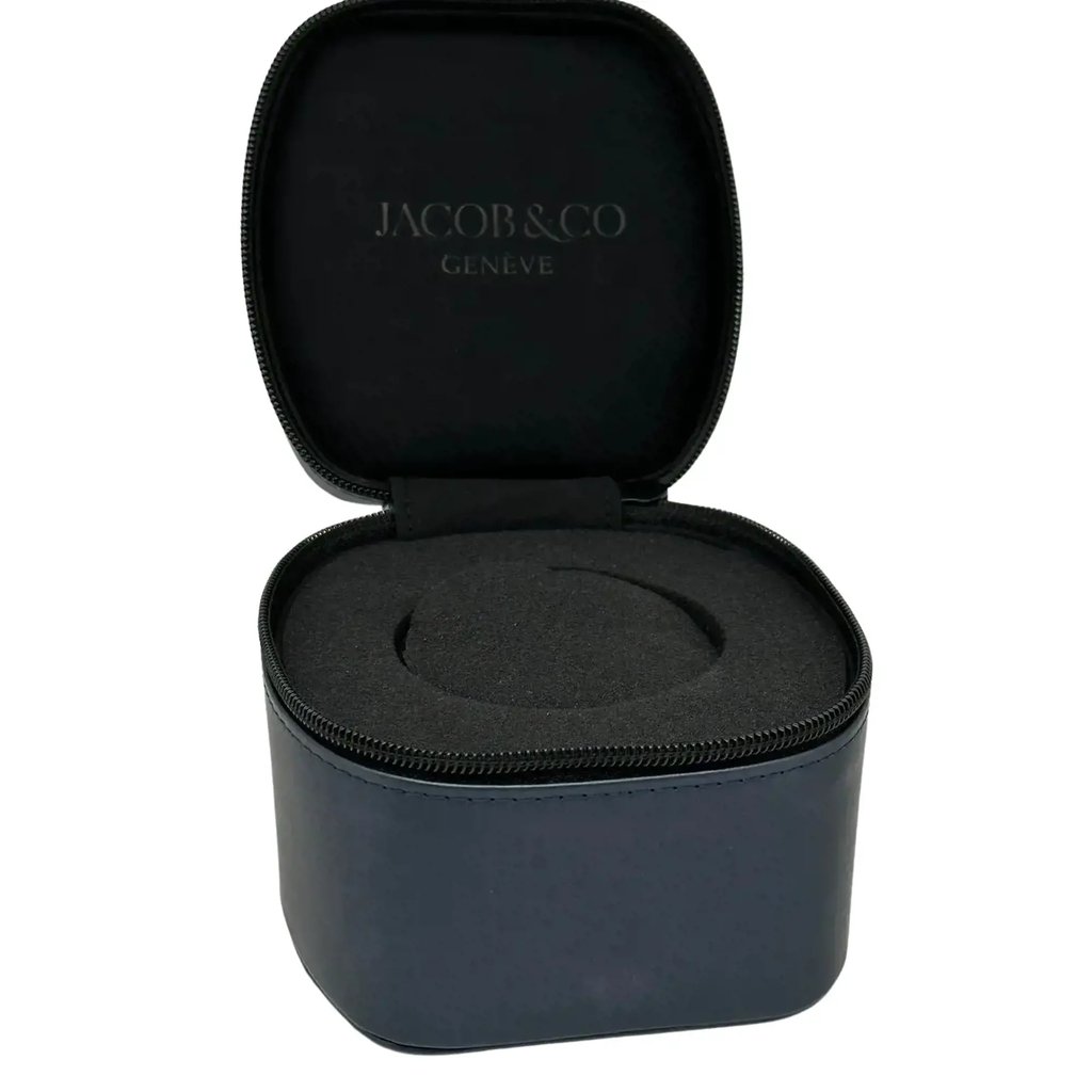 An image of a wristwatch box, positioned centrally and captured at a slight angle from the front. The box is open, showing a dark, cushioned interior designed to hold a watch. The brand name "Jacob & Co Genève" is visible on the inside of the lid. The box is situated against a plain background, with a close-up view focusing on the box itself.