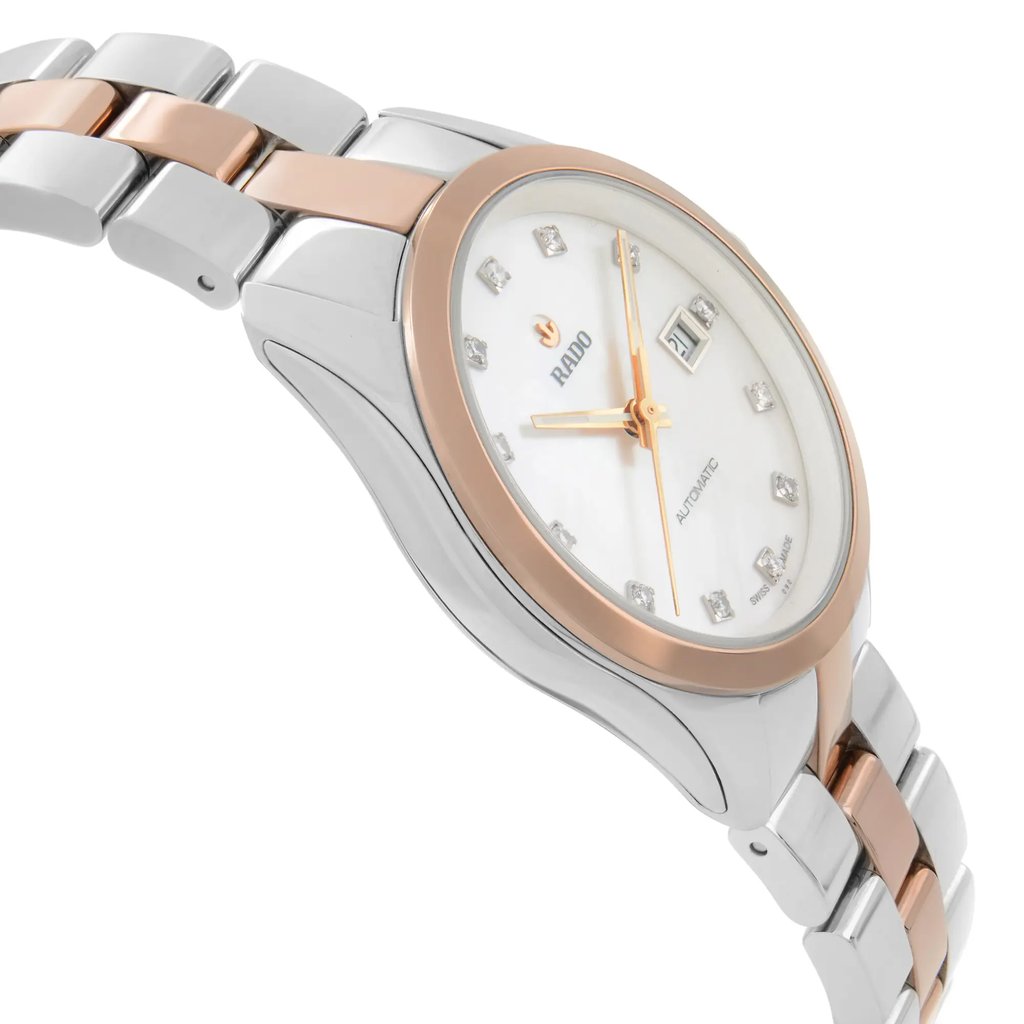 An image of a wristwatch taken from the side profile view, opposite the crown. The watch is a display model, showcasing a two-tone metal bracelet with silver and rose gold links. The angle highlights the watch's face with a rose gold bezel, white dial, and diamond-like hour markers. The distance provides a clear, detailed view of the watch's elegant design and craftsmanship.
