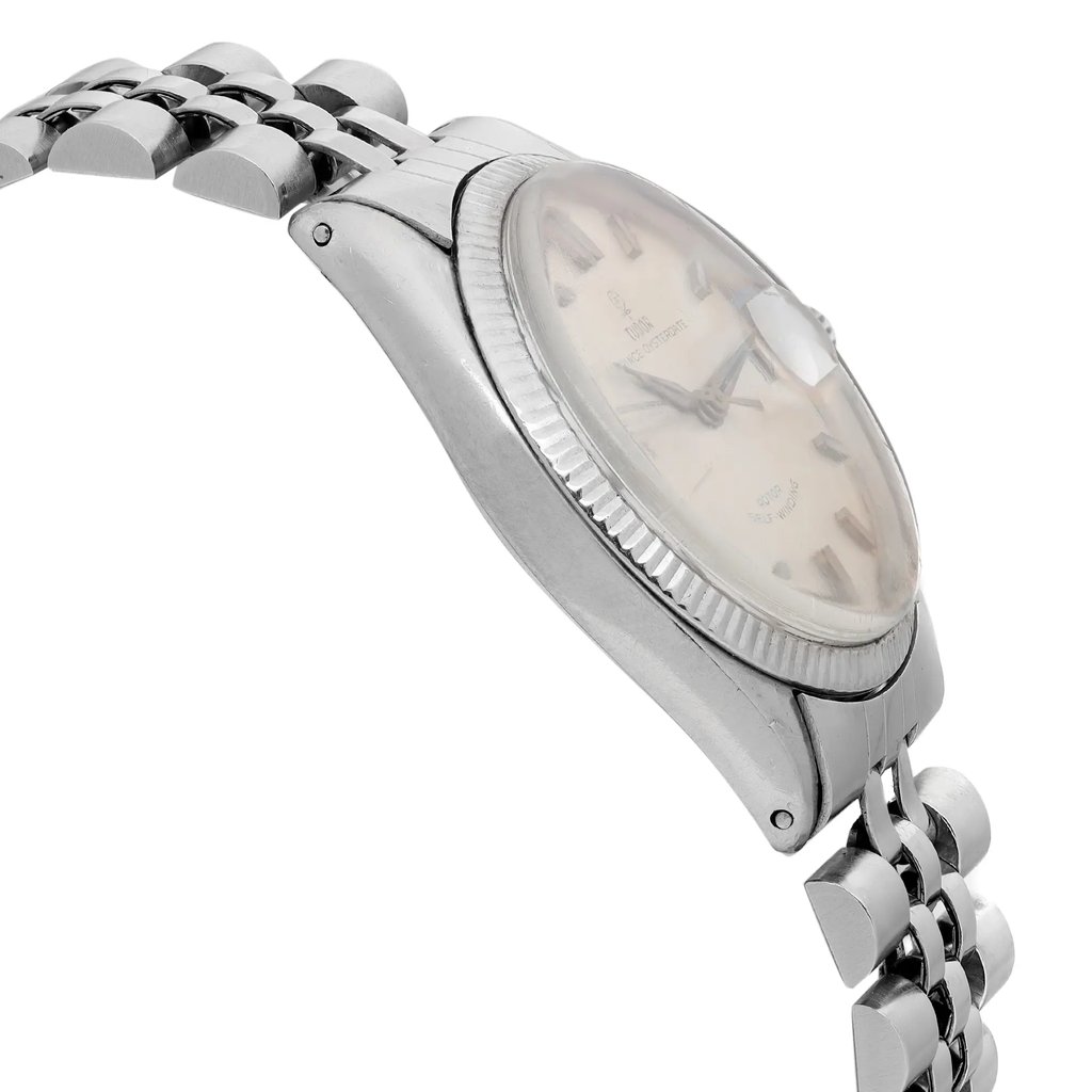 An image of a pre-owned men's TUDOR wristwatch, viewed from a side angle. The watch features a white gold case and a linked bracelet. The face of the watch, which includes a date indicator, is seen at a slight angle, highlighting its domed glass and classic design. The photograph is taken at a close distance, focusing on the watch's profile and bracelet details.