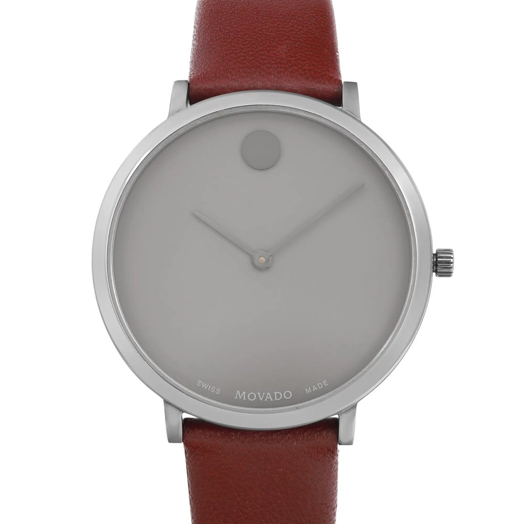 An image of a pre-owned wristwatch taken from a front close-up angle, showcasing the watch face. The watch features a minimalist design with a silver-toned case and a single dot at the twelve o'clock position. The hands are slim and the dial is plain without numerals. The brown leather strap is partially visible, attached to the case. The brand name "Movado" is subtly displayed on the bottom of the face.