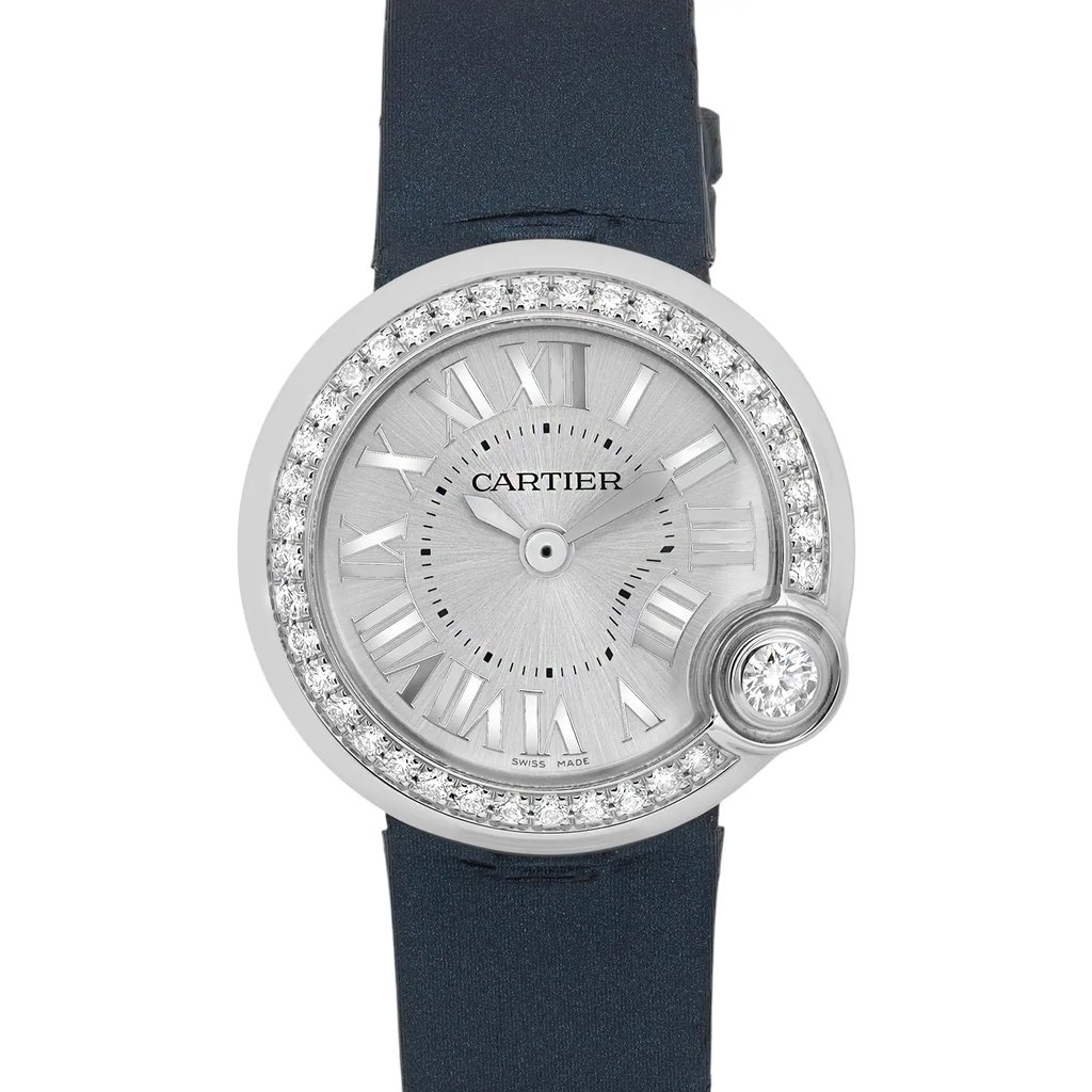 An image of a pre-owned women's Cartier wristwatch viewed from a straight-on angle, showcasing its elegant design. The watch features a round silver-tone face with Roman numeral hour markers and a diamond-encrusted bezel. The strap is a dark blue color, and the image is captured at a close distance to highlight the intricate details and craftsmanship.