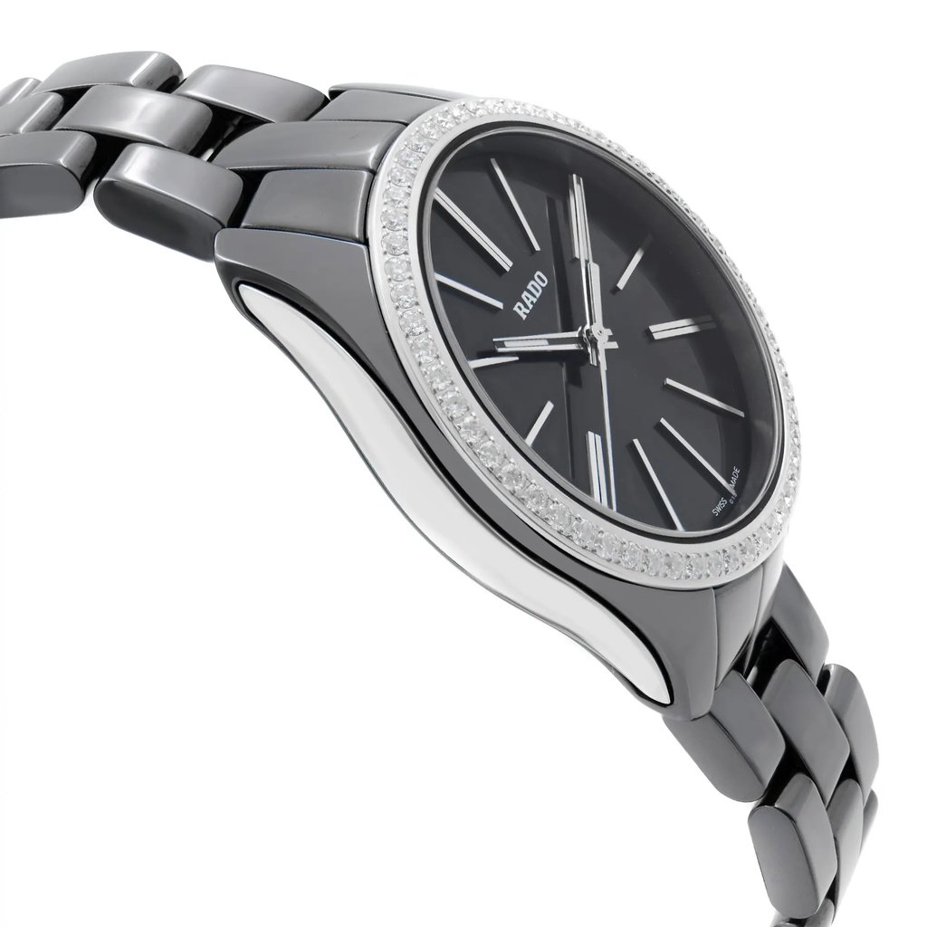 An image of a wristwatch taken from a side profile view, highlighting the opposite side of the crown. The watch is a display model, showcasing a sleek metal bracelet and a round, polished bezel adorned with crystals. The dial is dark with minimalistic hour markers and hands. The angle emphasizes the watch's contours and the seamless integration of the bracelet, photographed from a close distance to capture the intricate details.