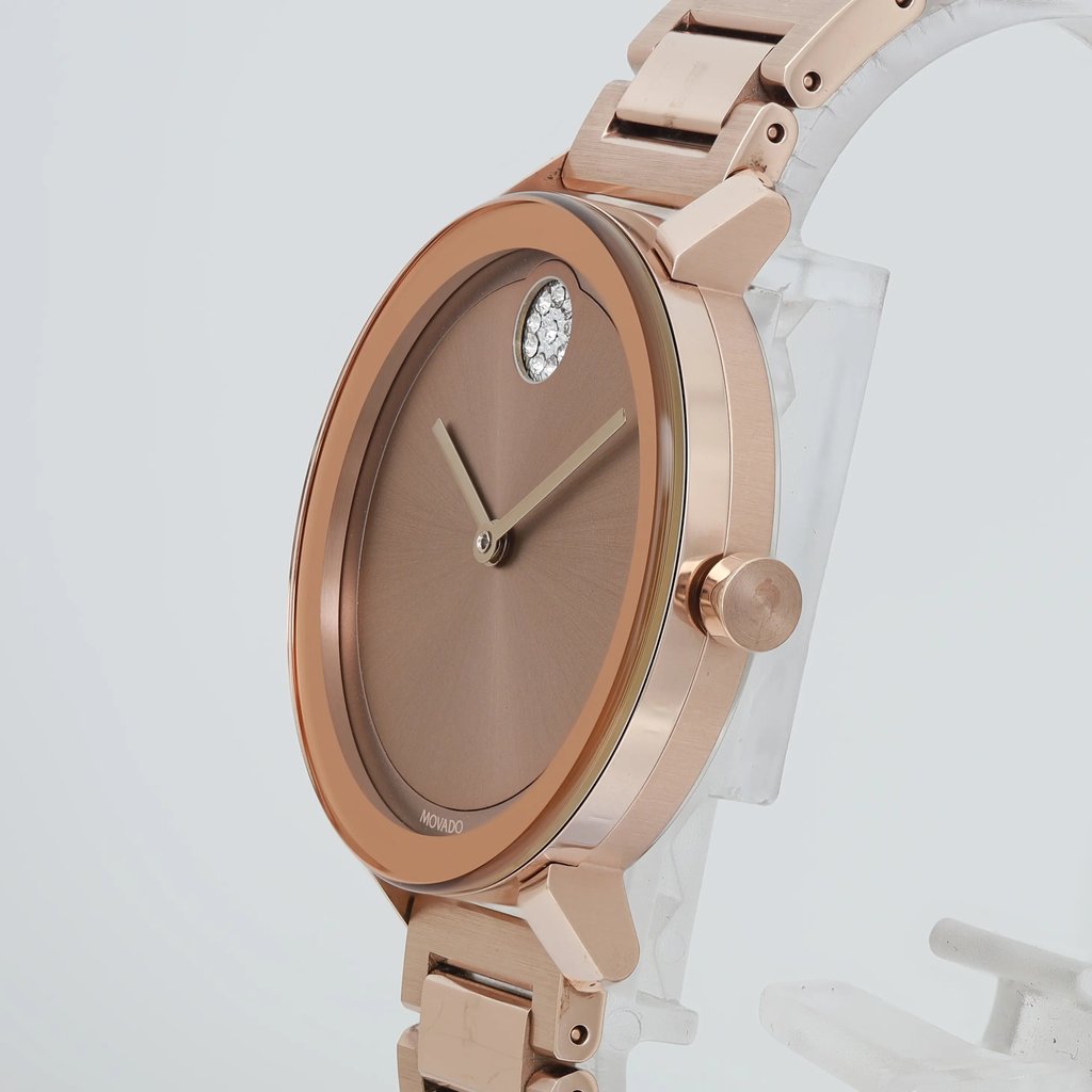An image of a pre-owned wristwatch captured from a side profile view at a close distance. The focus is on the rose gold-colored case and bracelet, with the crown prominently visible. The watch face is a matching bronze hue, featuring minimalistic hands and a single diamond accent at the 12 o'clock position. The overall angle highlights the watch's sleek design and elegant finish.