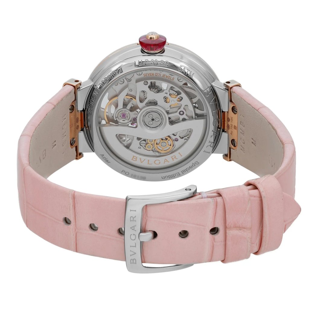 An image of a pre-owned wristwatch shown from the back view with a focus on its open clasp. The watch features a transparent case back revealing intricate internal mechanisms. It has a pink leather strap and a silver buckle with the brand name engraved. The shot is taken from a close distance, capturing the details of the watch's components and strap texture at a straight angle.