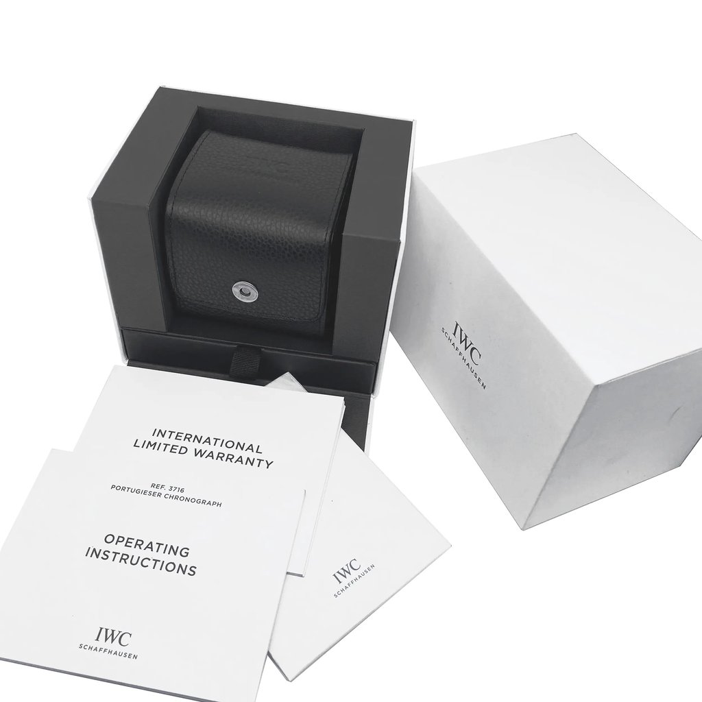 An image of an unworn IWC men's wristwatch box and documents, presented without the watch itself. The box, positioned in the center, is open, showcasing a black leather cushion intended for the watch. To the right, there's a white outer box with the IWC logo. In the foreground and various documents.