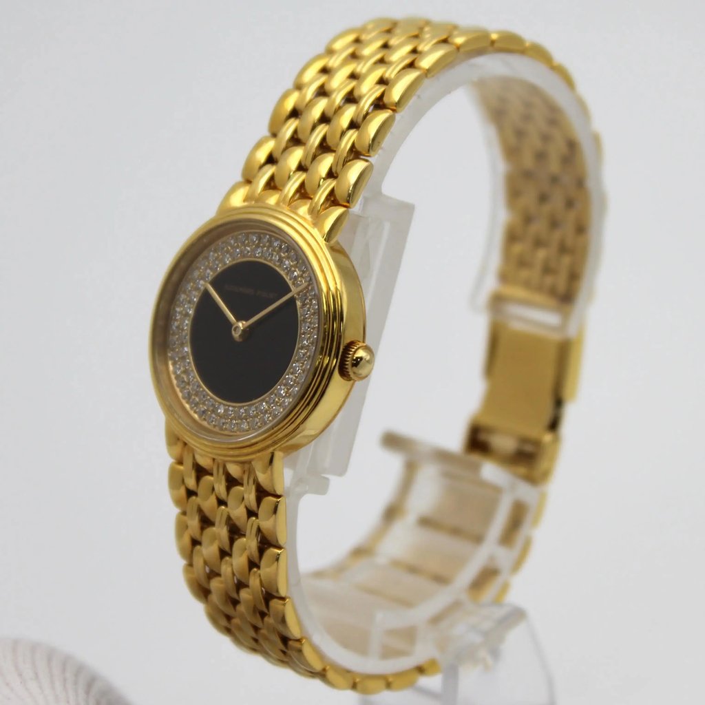 An image of a pre-owned Audemars Piguet women's wristwatch positioned at a slight angle, showcasing the right side and front. The watch features a yellow gold bracelet with a onyx face encircled by a diamond-studded bezel. The watch is displayed on a transparent stand, with the background softly blurred, highlighting its luxurious design.
