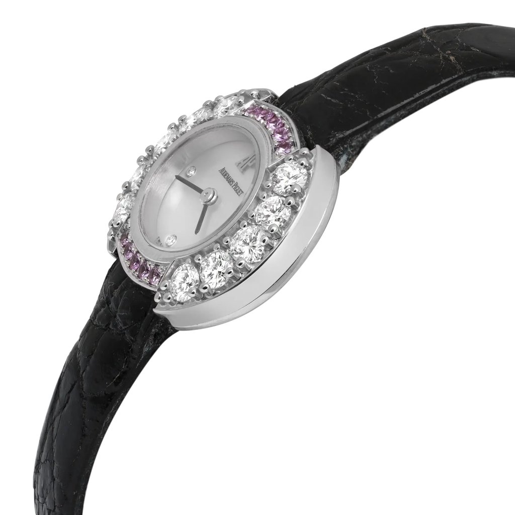 An image of a pre-owned women's Audemars Piguet wristwatch, taken from a close-up side angle. The watch features a round face with a mother of pearl dial, adorned with sparkling diamonds and gemstones around the bezel. The watch is set against a black leather strap, showcasing its elegant and luxurious design.