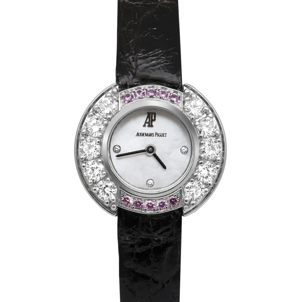 An image of a pre-owned Audemars Piguet women's wristwatch taken from a front-facing angle. The watch features a round face with a mother-of-pearl dial and is embellished with sparkling gemstones around the bezel. The watch hands are black, and the strap is made of black leather. The image captures the watch in a close-up view, highlighting its elegant design and luxurious details.