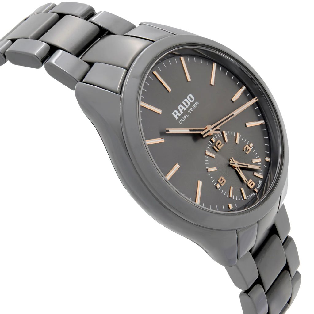 An image of a wristwatch viewed from a side profile angle, opposite the crown. The watch is positioned slightly tilted, showcasing its sleek design. It is a display model with a glossy finish and a metal link bracelet. The timepiece features a dual timer function with a dark dial and gold-toned hour markers and hands. The photograph is taken from a close distance, highlighting the watch's details and craftsmanship.