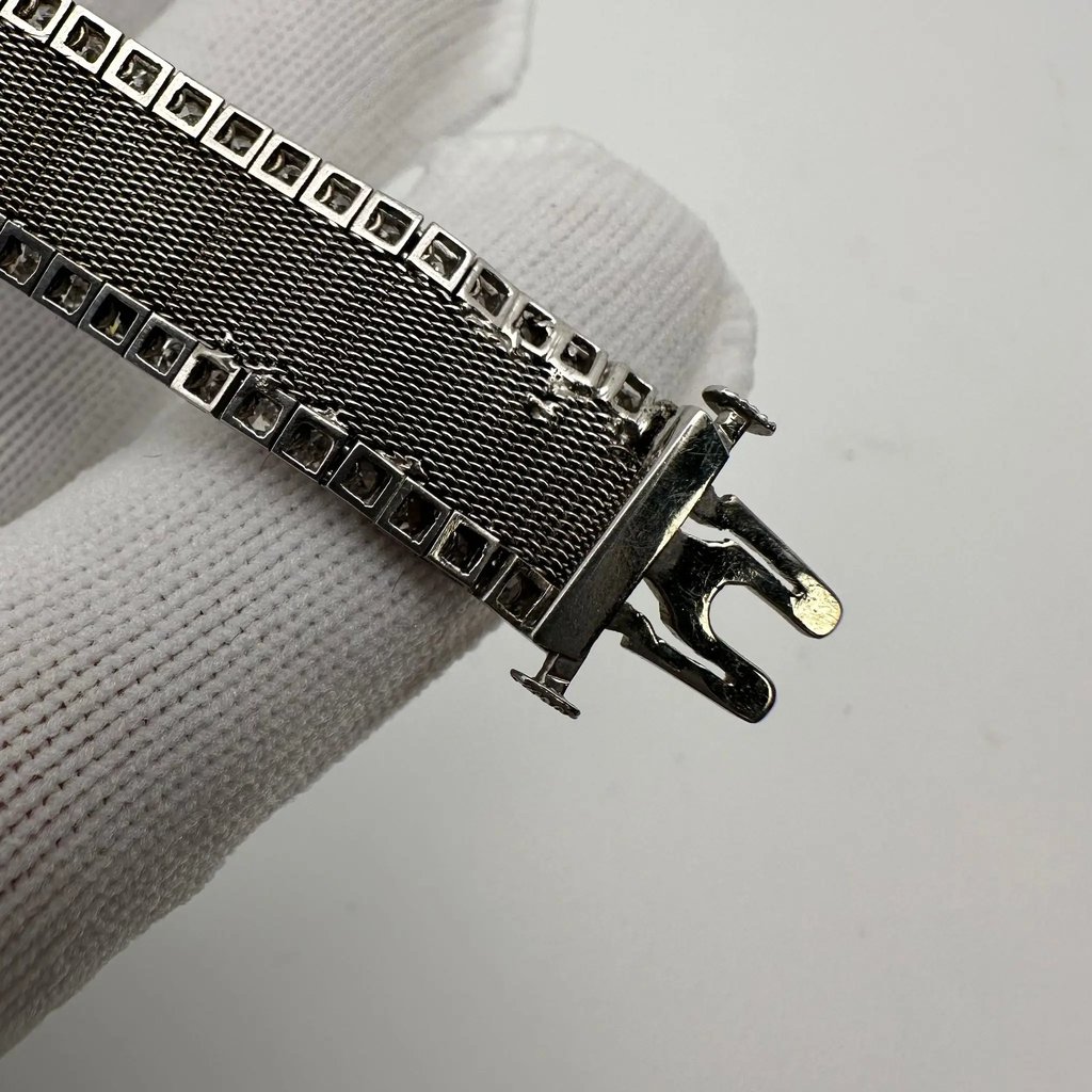 An image of a pre-owned Tissot women's wristwatch, focusing on the clasp and mesh band. The photo is taken at a close distance, angled to show the side of the clasp mechanism and the texture of the mesh band. The clasp is in an open position and exhibits signs of wear and damage, particularly on the metal mesh band which appears frayed at the edges.
