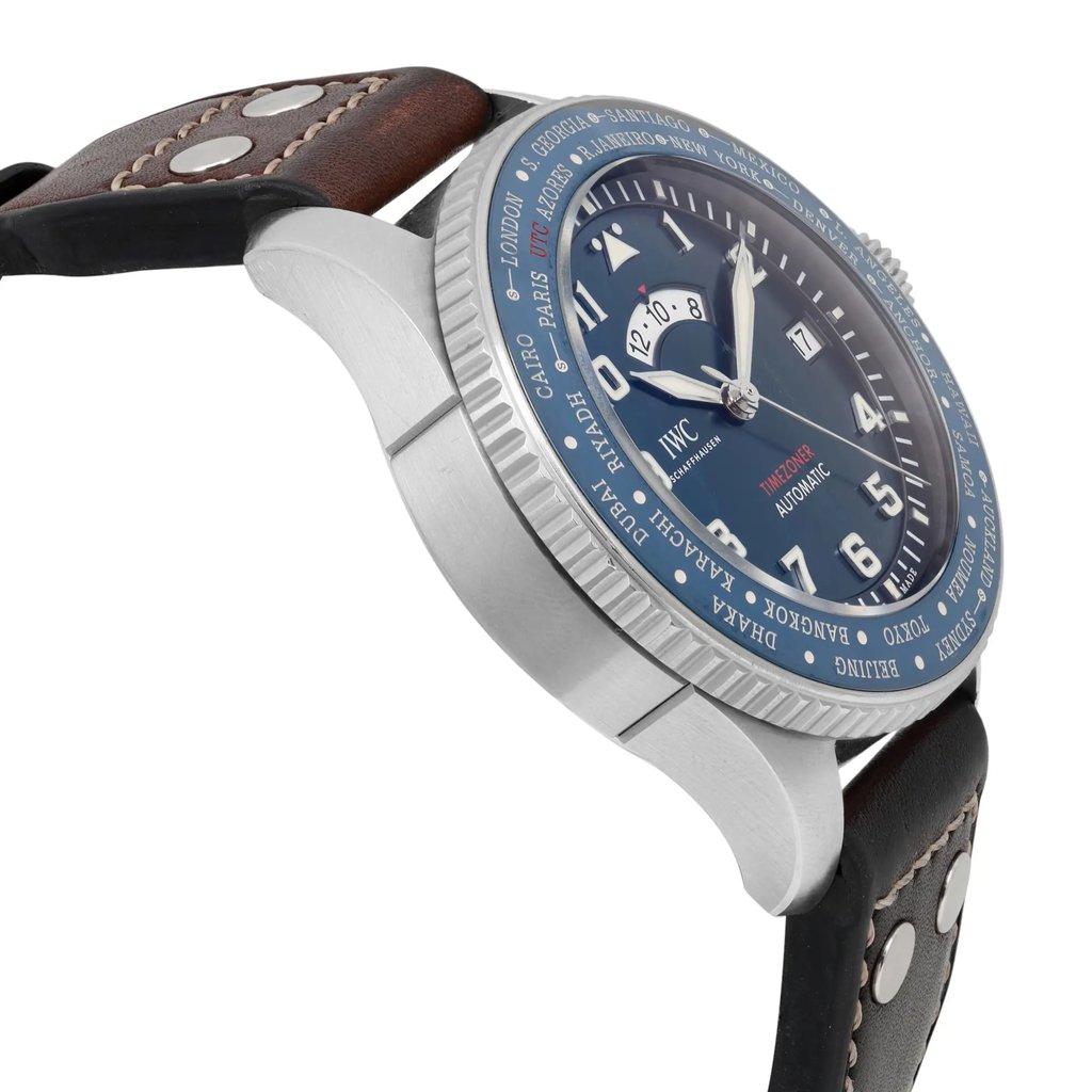 An image of a pre-owned IWC Timezoner Le Petit Prince Edition men's wristwatch taken from a side angle, showcasing the watch's metallic case and blue dial. The watch features luminous hands and a detailed world time zone bezel. The brown leather strap is visible, highlighting the stitching and metal rivets. The image provides a close-up view, capturing the intricate design and craftsmanship of the timepiece.
