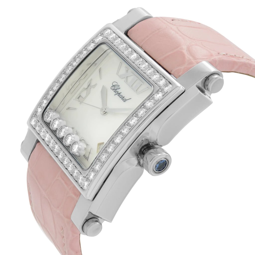 An image of a pre-owned wristwatch displayed from a side profile view, highlighting the crown. The watch features a rectangular face with a polished metal casing adorned with sparkling stones around the bezel. Its strap is a light pink color, resembling an alligator pattern. The watch face displays elegant Roman numerals and a brand name, with small decorative elements, creating a luxurious appearance. The angle captures the watch at a close distance, emphasizing its intricate details and craftsmanship.