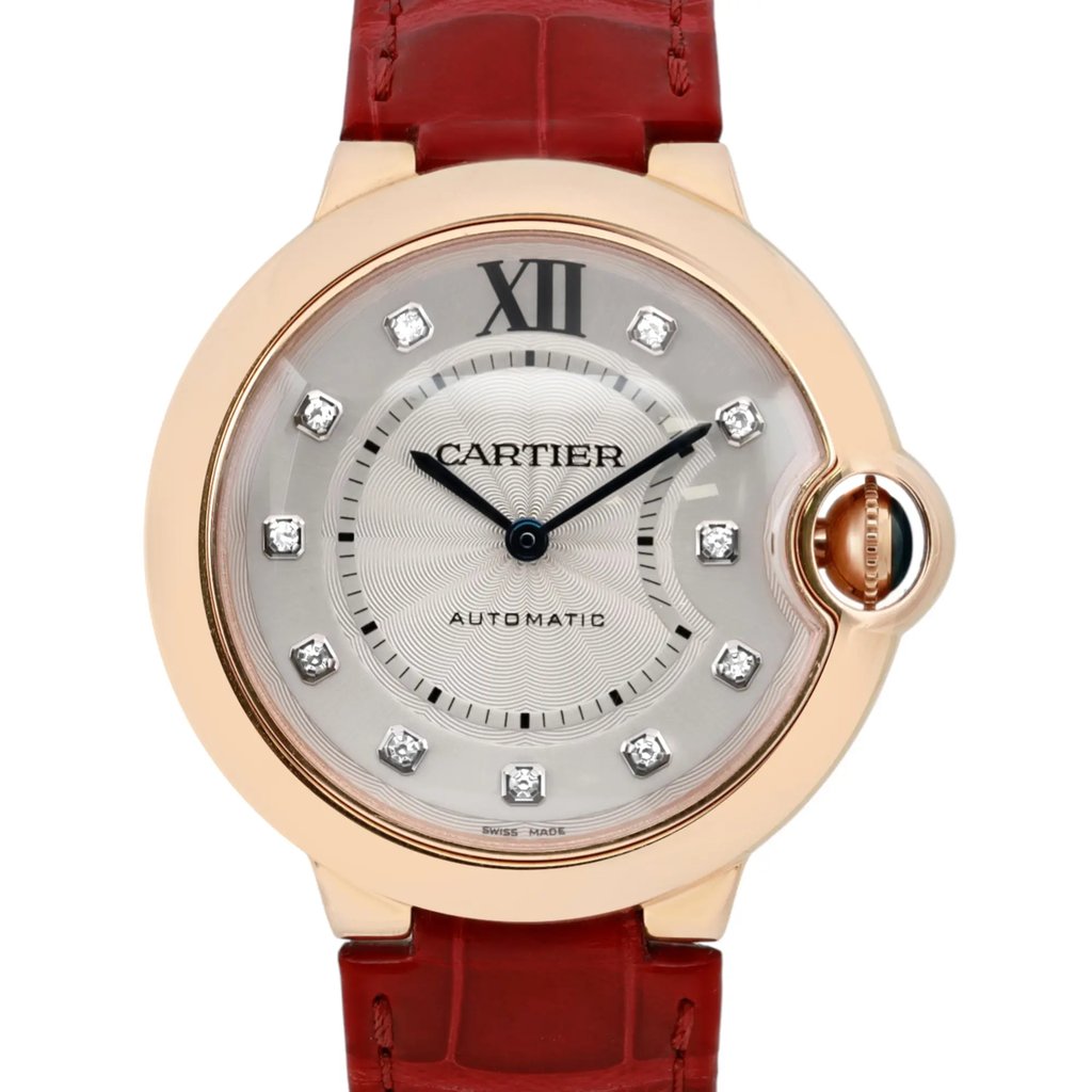 An image of a pre-owned Cartier women's wristwatch captured from a front-facing angle at a close distance. The watch features a round face with a rose gold bezel and a silver-toned dial adorned with diamond hour markers. The watch hands are elegantly styled in a blue tone. It has a distinctive crown guard on the right side, and the strap is crafted from red leather, adding a touch of luxury to the timepiece.