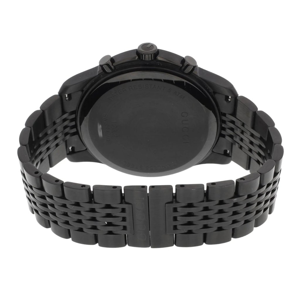 An image of a pre-owned Gucci men's wristwatch, viewed from the back. The stainless steel caseback with the Gucci branding is centered and in focus, showing a snap closure. The round shape of the watch is visible, and the stainless steel band with a double-locking fold-over clasp extends to the left and right sides of the frame. The photograph is taken from a close distance, with the watch positioned horizontally, capturing the entirety of the back and partial views of the band at a flat angle.