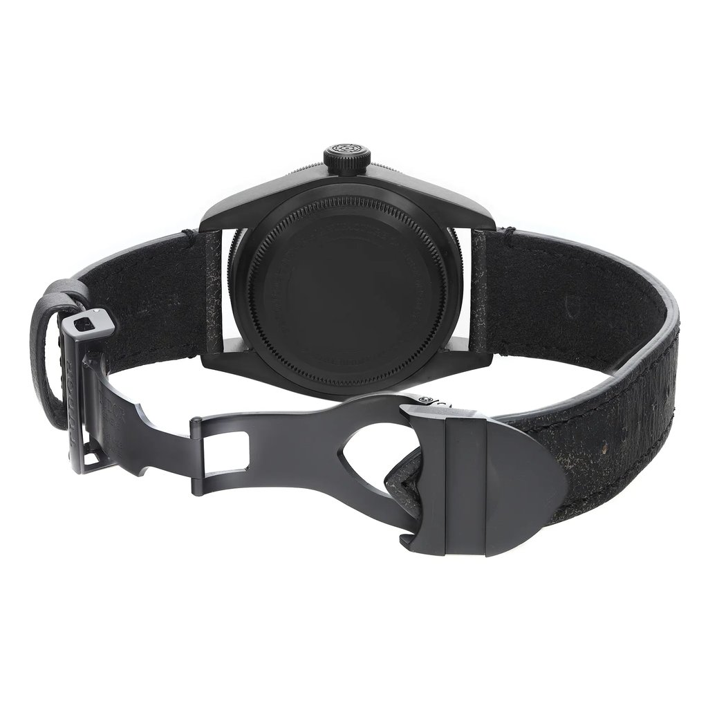 An image of a wristwatch taken from the back view, showcasing the open clasp. The watch is positioned centrally, with the focus on the circular back case and the open metal clasp beneath it. The angle provides a clear view of the textured black strap and the clasp mechanism. The image appears to be captured at a close distance, highlighting the watch's details and condition as a display model.