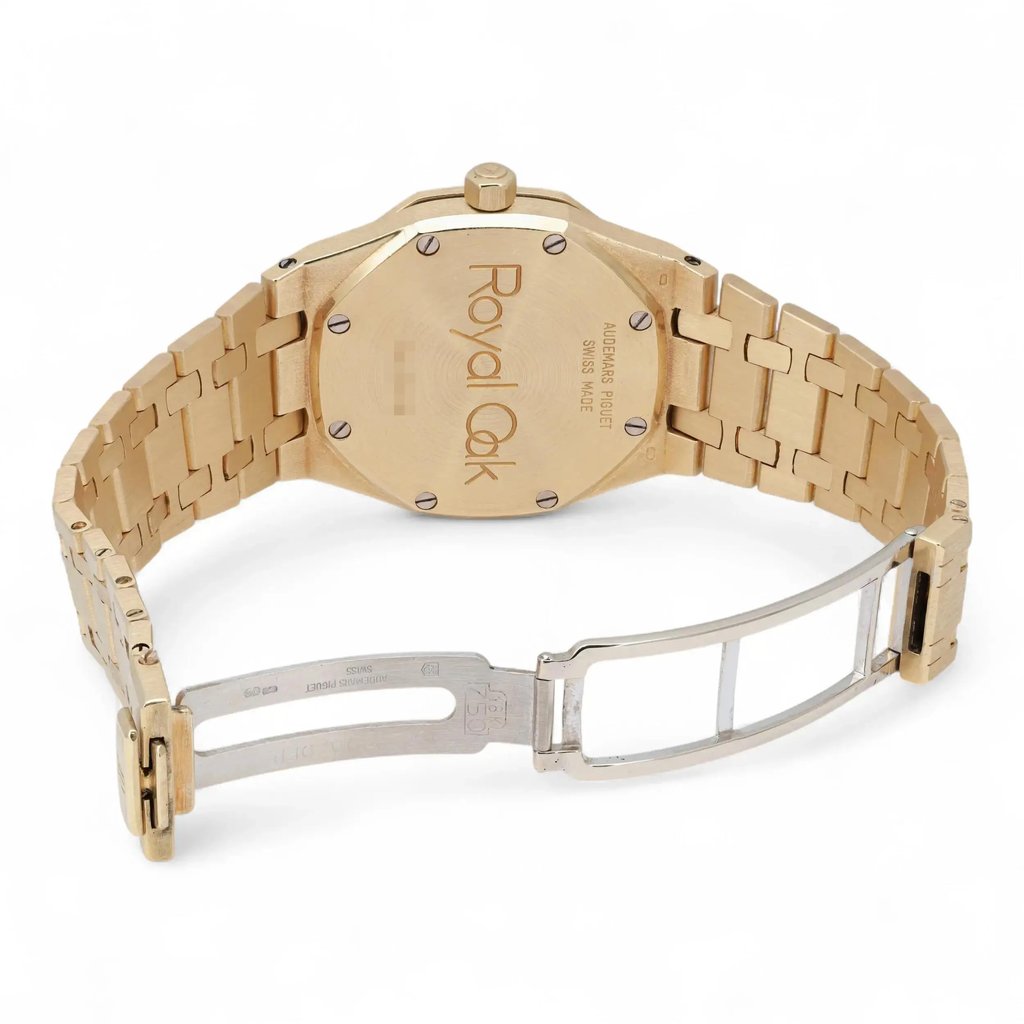 An image of a pre-owned Audemars Piguet women's wristwatch, featuring a date indicator. The watch is positioned with its case back facing the viewer, showcasing the "Royal Oak" engraving. It is angled slightly from above, highlighting the yellow gold bracelet and open clasp. The image is taken at a close distance, capturing the intricate details of the watch's links and clasp mechanism.