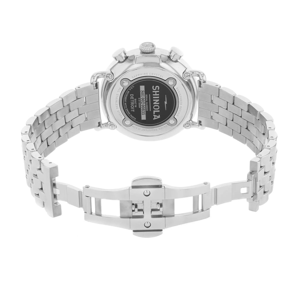 An image of a pre-owned wristwatch showcasing the back view with an open clasp. The watch is positioned centrally, with the camera capturing it from a straight-on angle, revealing the intricate details of the metal bracelet and the back casing. The image is taken at a close distance, emphasizing the brand name and serial number visible on the back of the watch.