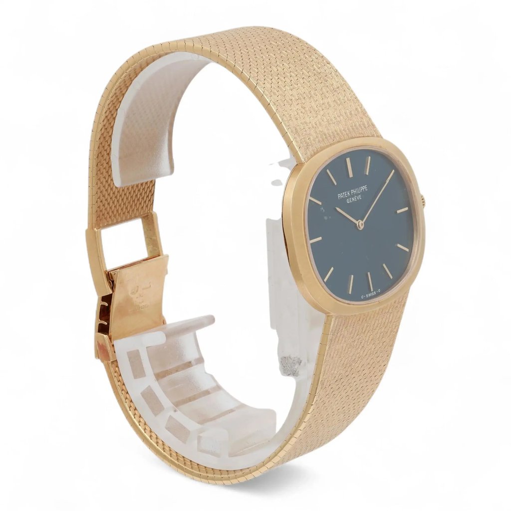 An image of a pre-owned Patek Philippe unisex adult wristwatch viewed from a three-quarter angle. The watch is positioned upright on a display stand, showcasing its elegant gold mesh strap and a blue, minimalist dial with simple hour markers. The image captures the watch from a close distance, highlighting its intricate design details.