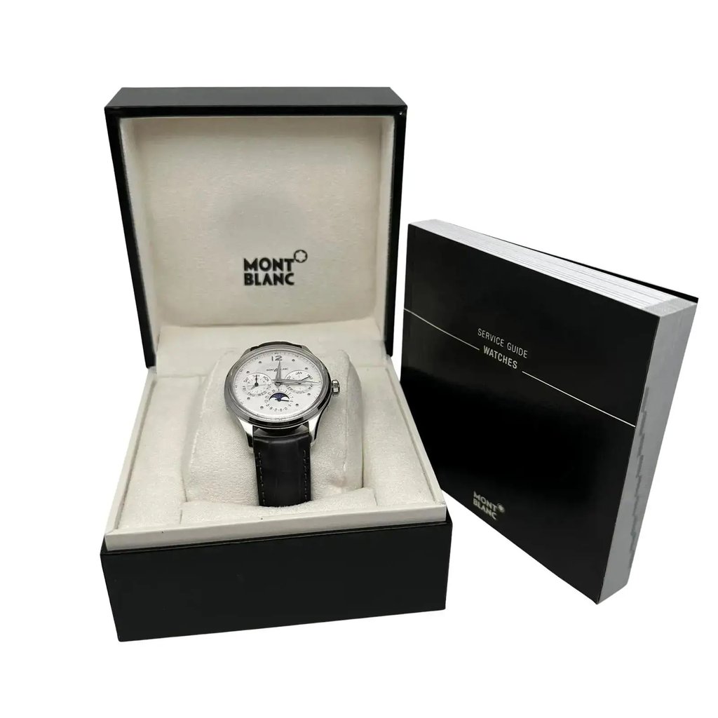 An image of a pre-owned Montblanc men's wristwatch presented in full view. The watch is centered and positioned at a slight angle to the left, showcasing its features like day/date, GMT, luminous hands, and moon phase on a white dial with black leather strap. It is displayed inside its original box with the Montblanc logo visible on the top interior, resting on a cushioned lining. To the right, partially out of the box, is a Montblanc service guide book for watches, suggesting the inclusion of original documents.