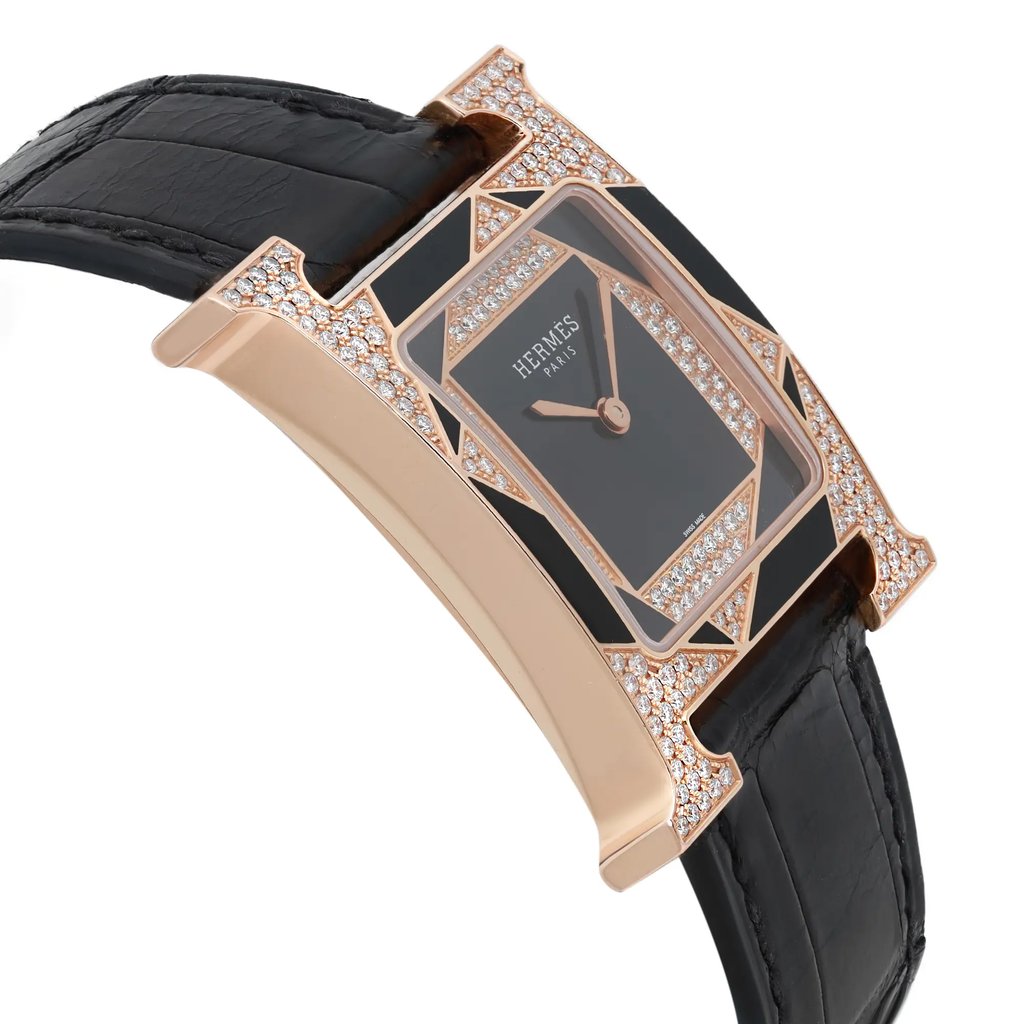 An image of a pre-owned women's Hermès wristwatch, captured from a slightly angled side view. The watch features a black leather strap and a rectangular face adorned with sparkling accents. The case is a polished metallic finish, creating an elegant contrast with the dark watch face, positioned to highlight its luxurious design. The angle showcases the intricate details of the watch's craftsmanship.