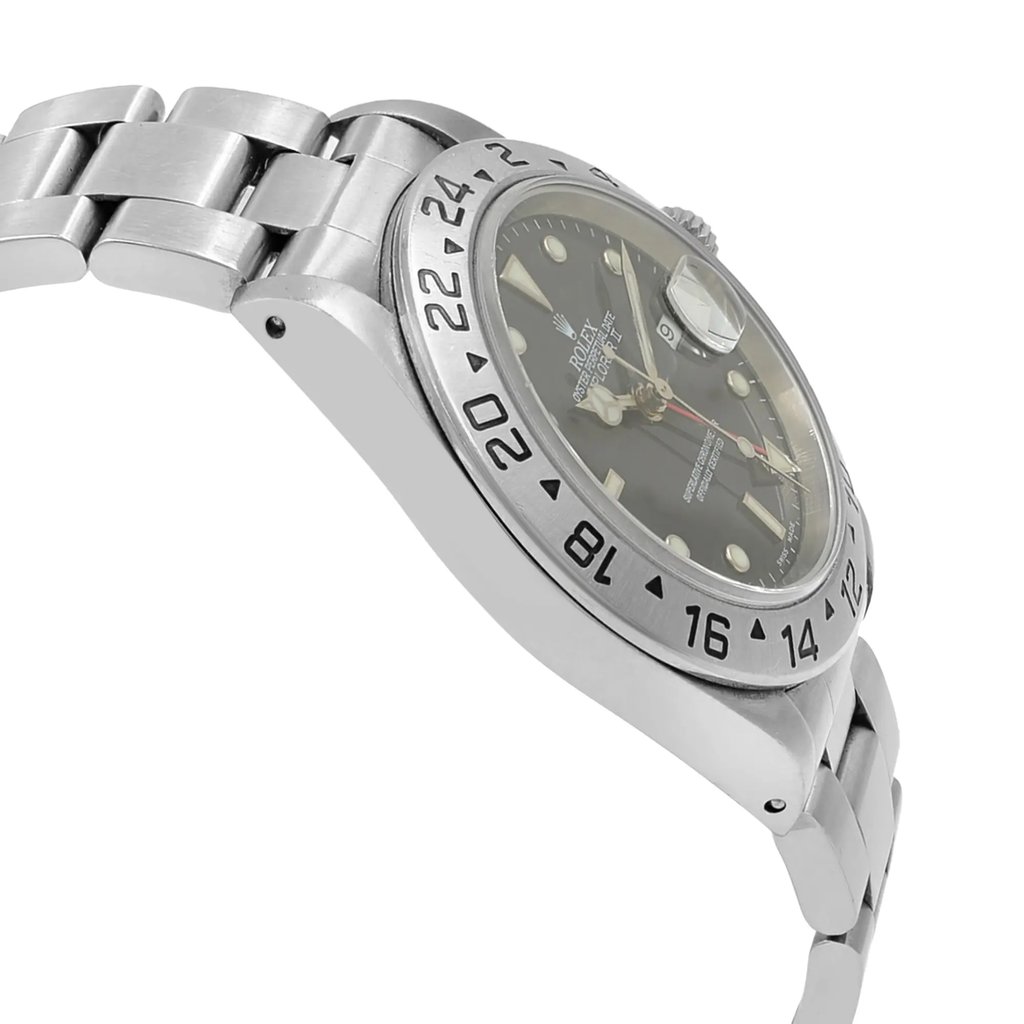 An image of a pre-owned wristwatch viewed from the side profile opposite the crown. The watch is angled slightly upward, showcasing the stainless steel case and bracelet. The focus is on the bezel, which is engraved with hour markers. The dial is partially visible, revealing a dark background with luminous indices and silver-toned hands. The photograph captures the watch at a close distance, highlighting its details and craftsmanship.