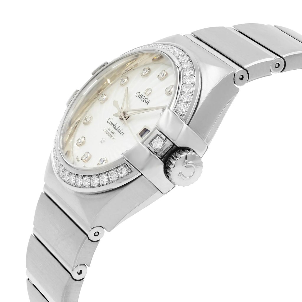 An image of a women's OMEGA wristwatch, showcasing a close-up side view from a slight angle. The watch features a white gold bracelet and a shimmering, diamond-studded bezel. The face is adorned with diamond hour markers and the brand's logo. The crown is visible on the right side, detailed with an embossed design. The watch is positioned at a medium distance, highlighting its elegant and luxurious design.