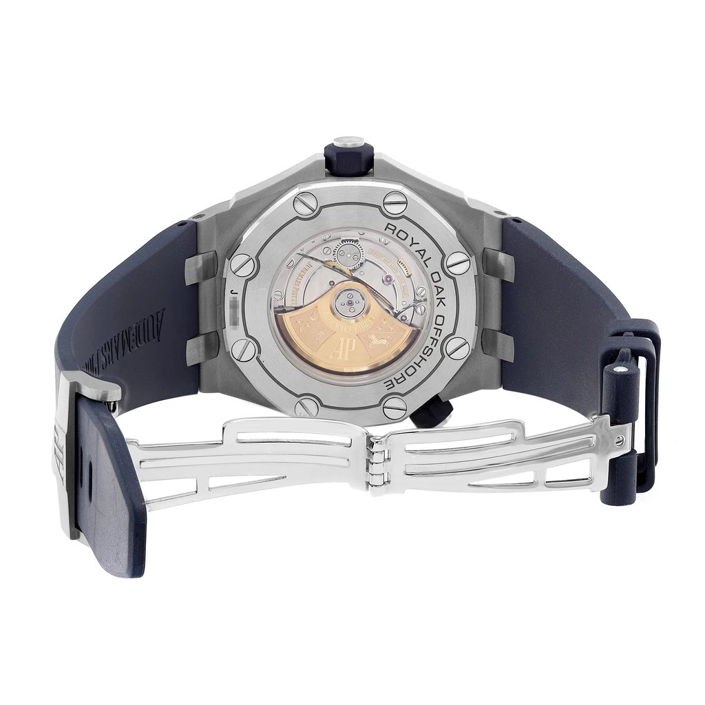 An image of a pre-owned wristwatch showing the back view with an open clasp. The watch is positioned at a slight angle, showcasing the intricate design of the exposed movement and the engraved brand name "Royal Oak Offshore" on the case back. The clasp is fully extended, emphasizing the metal links and the navy blue strap. The photo is taken from a close distance, highlighting the details of the watch's craftsmanship.