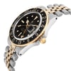 An image of a pre-owned wristwatch shown from a side profile view. The gold crown is prominently visible on the right side. The watch features a black dial with gold accents and a two-tone metal bracelet. The angle highlights the watch's thickness and the curvature of the bracelet, captured from a moderate distance.