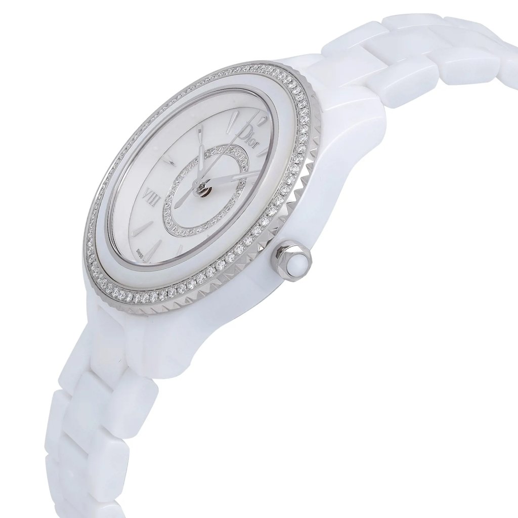 An image of a luxury women's wristwatch from Dior, shown from a side profile view. The crown is visible, positioned on the right side of the round ceramic case. The watch has a white mother of pearl dial with a gray bezel and features luminous hands. The ceramic band is visible, and the watch is a display model. The angle and distance highlight the elegant design and materials.