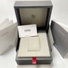 An image of an Oris wristwatch display box and accompanying documents. The box is open, showcasing a padded watch holder inside. Positioned centrally is a branded card with the Oris logo. Surrounding the box are various manuals, including an International Service Centers booklet on the left and a Product Manual on the right. The photo is taken from a slightly elevated angle, capturing the full view of the box and documents at a close distance.