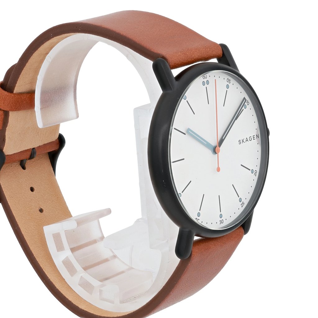 An image of a Skagen men's wristwatch, positioned at a three-quarter angle from the front. The watch features a brown leather strap and a minimalist white dial with luminous hands. The timepiece is displayed on a clear stand, emphasizing its sleek design.
