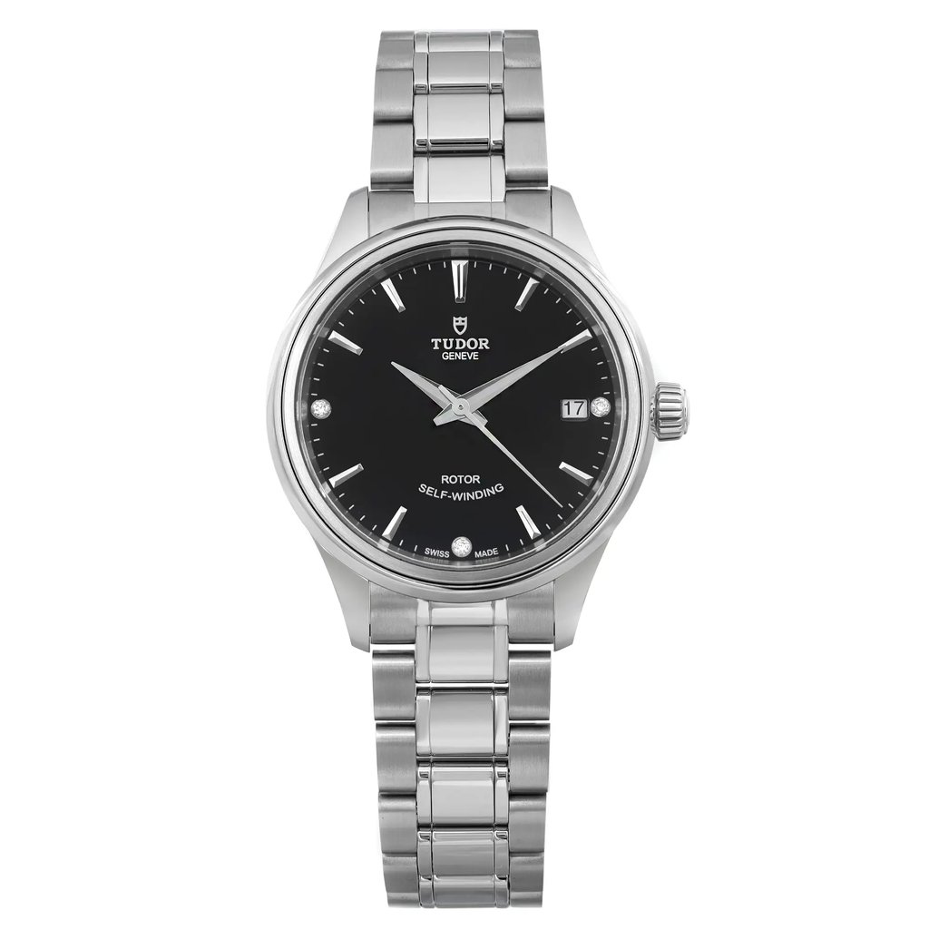 The image presents a close-up, straight-on view of a ladies' TUDOR Style 34mm wristwatch. This watch boasts a sleek diamond black dial with a date indicator located at the 3 o'clock position. The unworn stainless steel bracelet and case display a polished finish. The brand name and the text "Rotor Self-Winding" can be seen on the dial.