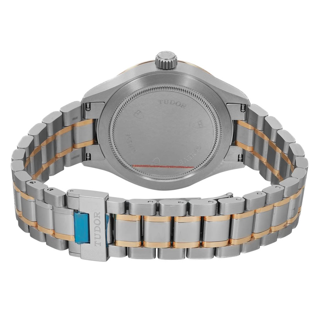 An image of a wristwatch taken from the back view, showcasing the closed clasp. The watch features a brushed silver case and a two-tone metal bracelet with alternating silver and gold links. The brand name "Tudor" is engraved on the clasp. The image is captured from a close distance, highlighting the unworn condition and fine details of the craftsmanship.