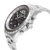 An image of a pre-owned Breitling luxury men's wristwatch with a side profile view showcasing the crown. The watch has a round stainless steel case and band, with a black dial featuring multiple subdials and a steel bezel. The watch is photographed at a close distance, highlighting the textures and details of the design, including the numerical hour markers and the Breitling logo on the crown. The watch is pre-owned and may show signs of wear and scratches.
