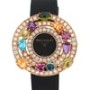 An image of a pre-owned Bvlgari women's wristwatch. The watch face is centrally positioned and viewed directly from the front. It features a black dial with the Bvlgari logo and is surrounded by a luxurious arrangement of colorful gemstones and two concentric circles of diamonds. The strap is black and partially visible at the top and bottom. The image captures the watch in close-up, showcasing its intricate details and vibrant colors at eye level.