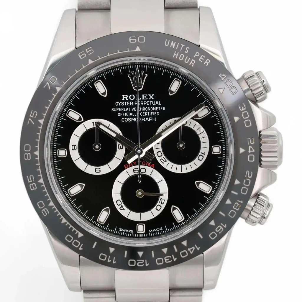 An image of a pre-owned men's Rolex wristwatch, viewed from the front at a slight angle. The watch features a stainless steel case and bracelet, with a black dial showcasing three subdials for the chronograph and small seconds functions. The luminous hands and markers stand out against the dial. The bezel is engraved with units per hour for tachymetric measurements. The image is taken at a close distance to highlight the intricate details of the watch's face and features.