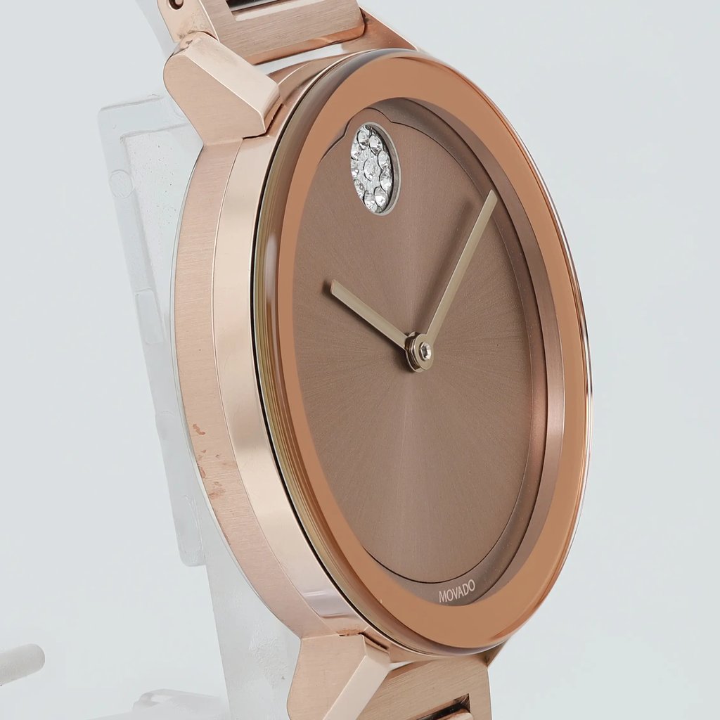 An image of a pre-owned wristwatch shown from a side profile view, opposite the crown. The watch features a rose gold-tone case with a smooth, round bezel. The face is a matching brown hue with minimalist hands and a small section of crystal detailing near the 12 o'clock position. The watch is positioned upright, angled slightly to the side, highlighting its sleek design and reflective surfaces at a close distance.