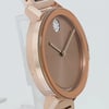 An image of a pre-owned wristwatch shown from a side profile view, opposite the crown. The watch features a rose gold-tone case with a smooth, round bezel. The face is a matching brown hue with minimalist hands and a small section of crystal detailing near the 12 o'clock position. The watch is positioned upright, angled slightly to the side, highlighting its sleek design and reflective surfaces at a close distance.
