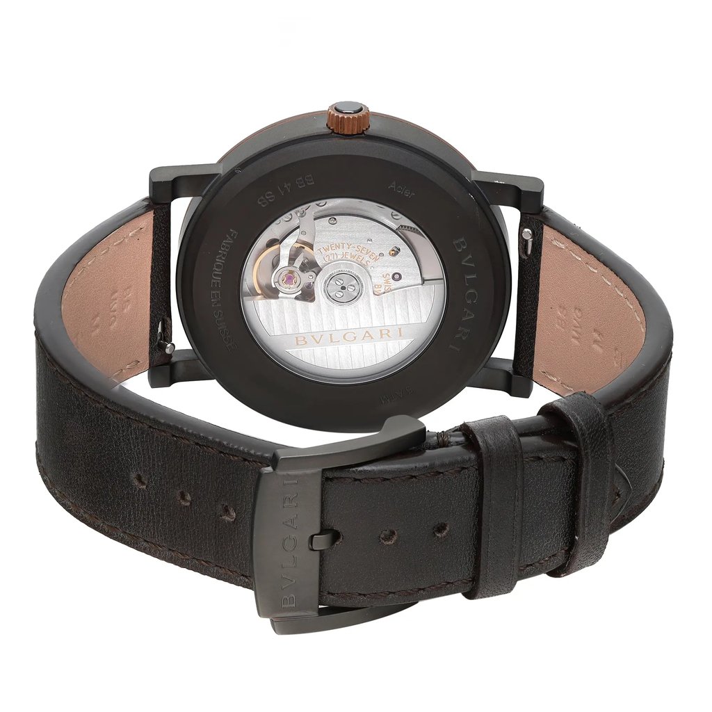 An image of an unworn Bvlgari men's wristwatch with a Black DLC stainless steel round case and an exhibition caseback, viewed from the back at a straight angle. The watch features a dark brown leather band with a buckle closure, and the clasp is in a closed position. The image is taken from a close distance, highlighting the craftsmanship of the watch and the branding on the caseback.