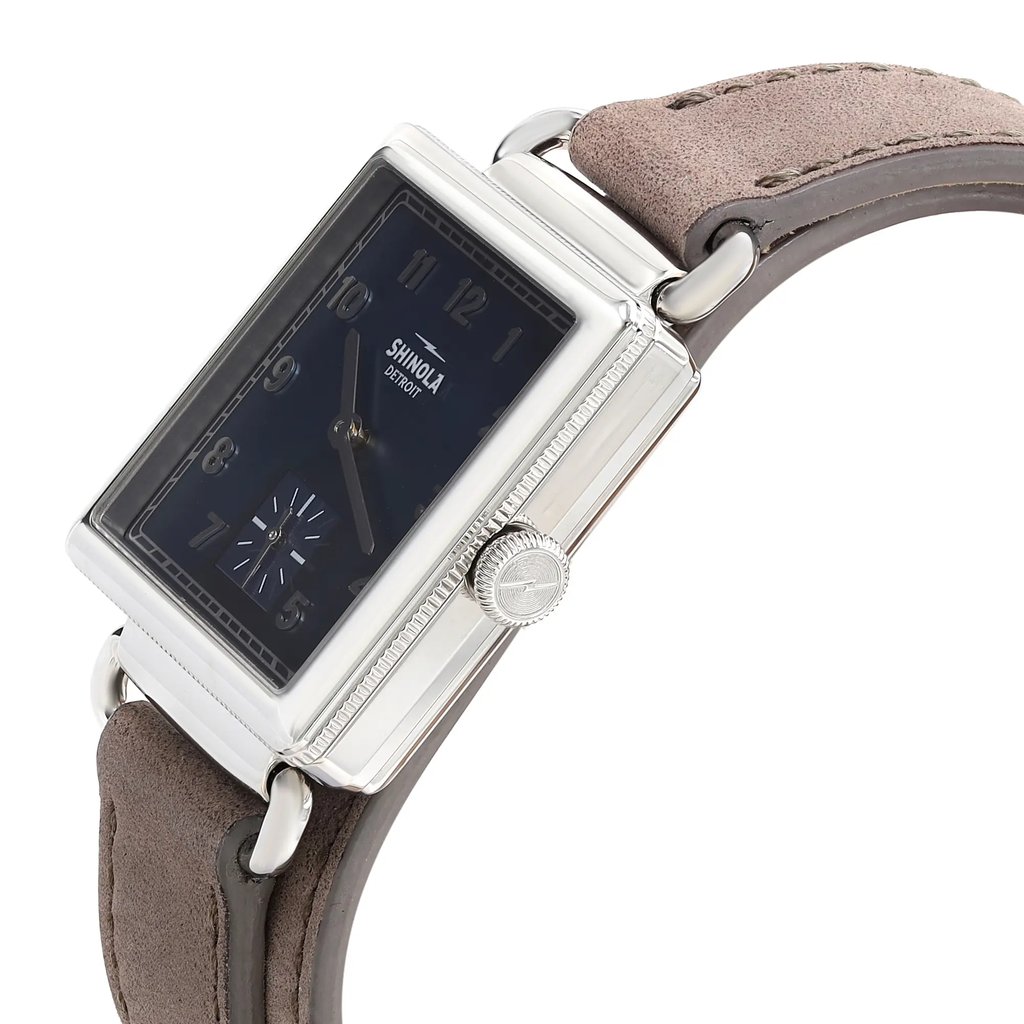 An image of a wristwatch taken from a side profile view, showcasing the crown prominently. The watch has a rectangular face with a dark dial and numerals. The case is metallic, and the band is made of brown leather. The display model is positioned at an angle, highlighting the watch's thickness and detailing from a close distance.