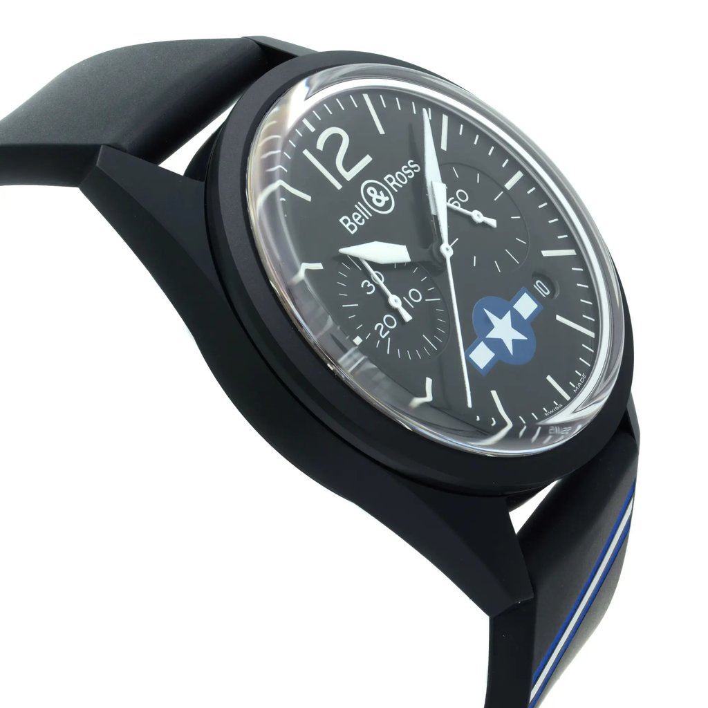 An image of a wristwatch at a close-up angle, predominantly displaying the face of the watch. The watch has a black strap with a blue accent line and a black casing. The watch face is black with white hour markers and numerals at 12 o'clock position. There are white hands for the hours and minutes, and a smaller sub-dial near the 3 o'clock position. The brand "Bell & Ross" is visible at the top of the watch face. The angle of the shot is slightly rotated, giving a view of the watch from a front-right perspective. Watch is unworn condition. 